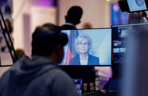 ﻿Christine Lambrecht ist auf einem Bildschirm zu sehen, der hinter den Gästen des Events steht. Es ist augenscheinlich die Regie.