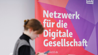 Frau guckt vor einem D21-Banner auf ihr Smartphone