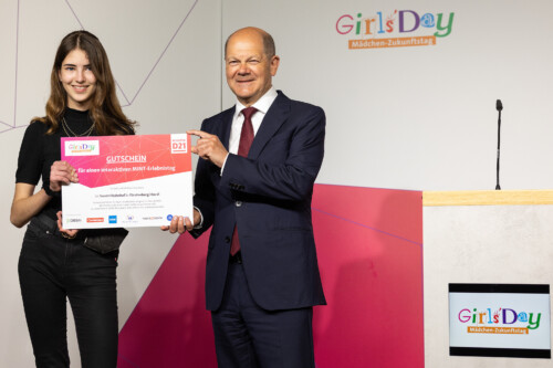 Bundeskanzler Scholz überreicht einen Gutschein an eine Schülerin
